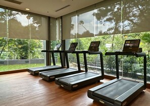 Four treadmills arranged in a row with a wooden floor, large windows, and a view of greenery outside. - Petaling Jaya Marriott Hotel (Petaling Jaya)