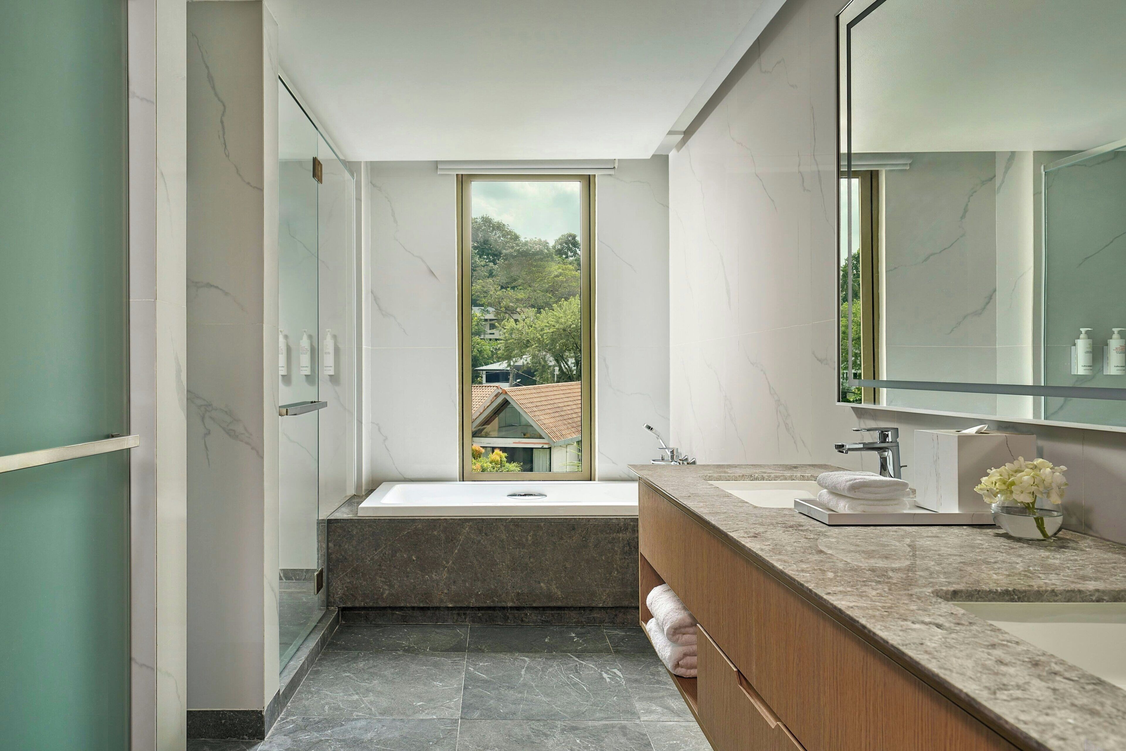 A modern bathroom with a large window, a bathtub, a vanity with a mirror, and a sink.