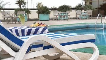 Ein Liegebereich am Pool mit einem gestreiften Handtuch, einem Getränk und einer Fruchtplatte.