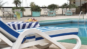 A poolside lounge area with a striped towel, a glass of drink, and a plate of fruit. - Safir International Hotel Kuwait (Kuwait City)
