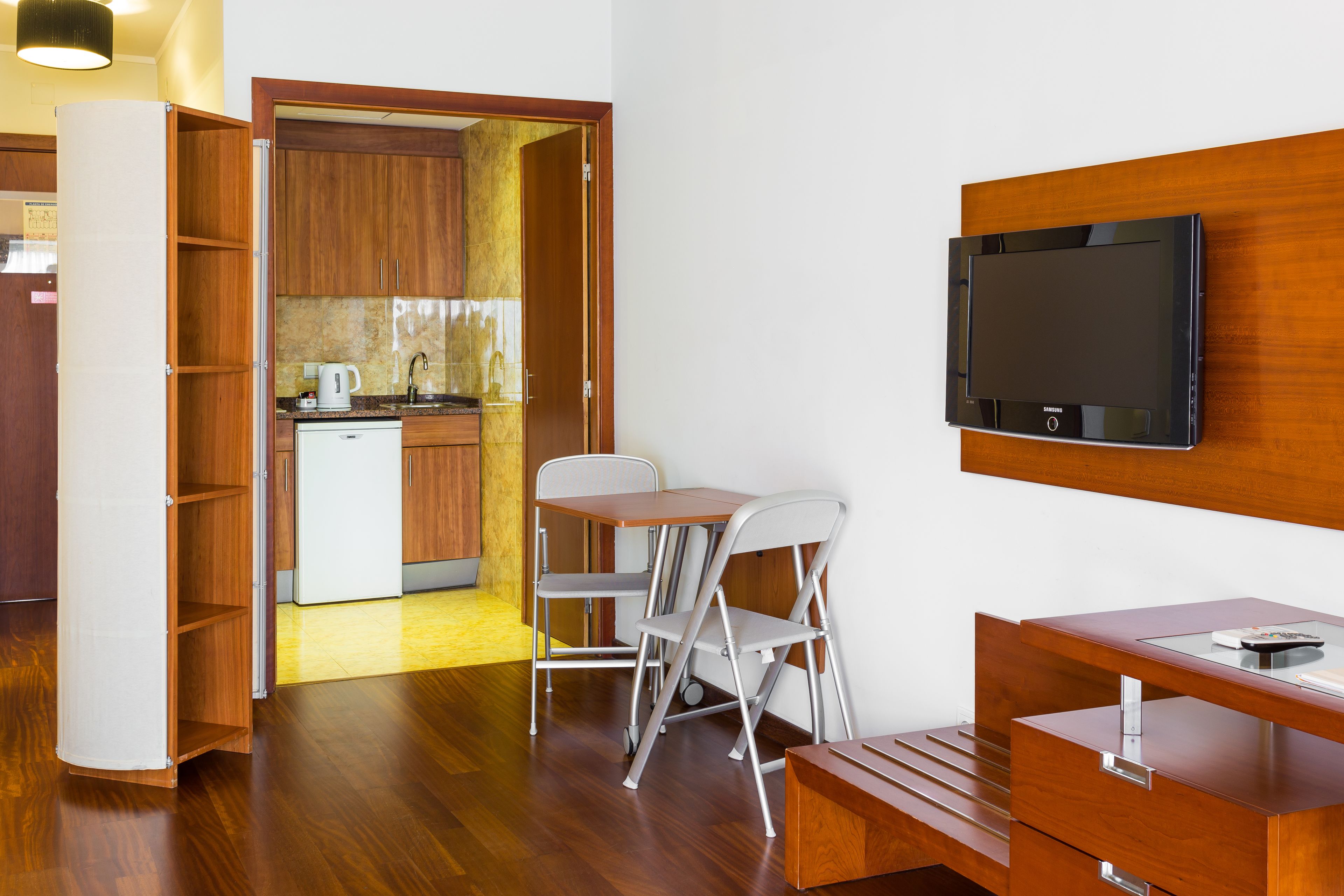Um espaço compacto com cozinha compacta, uma mesa dobrável, televisão na parede e um armário de madeira.