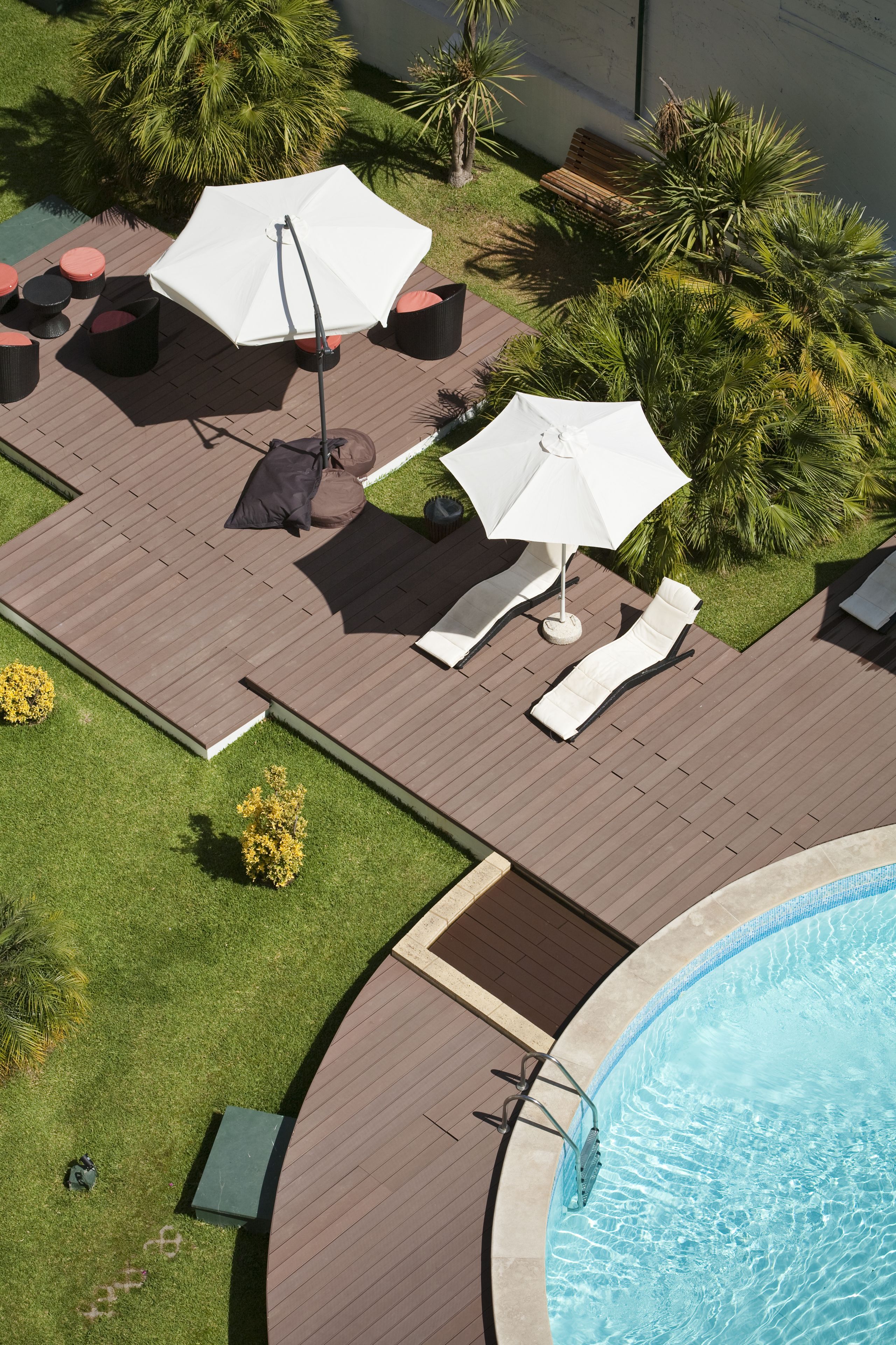 A rooftop pool area with lounge chairs and umbrellas, surrounded by greenery and a wooden deck.
