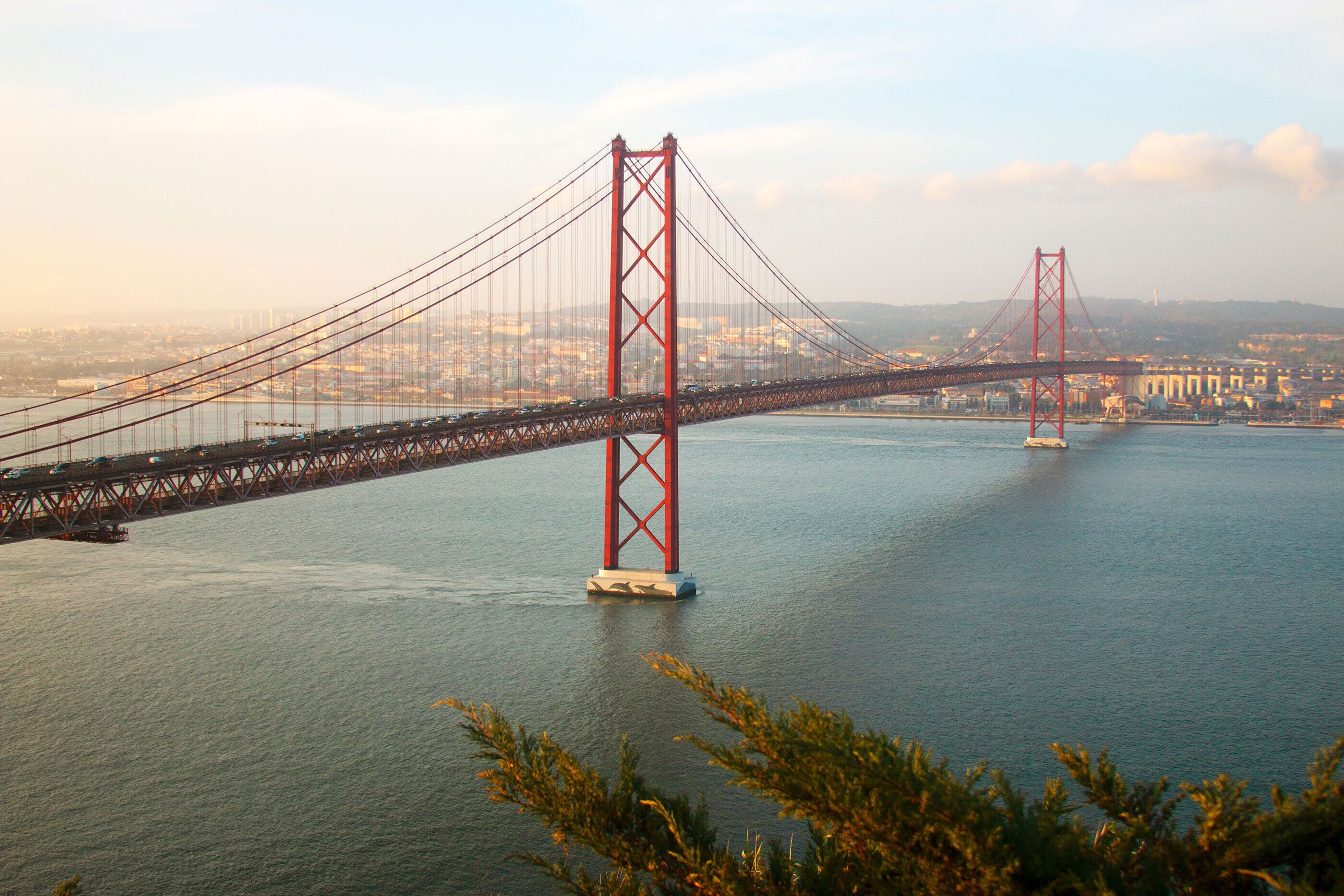 A large suspension bridge spanning a wide body of water with a cityscape in the background.