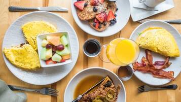 A breakfast setting with various dishes including pancakes, waffles, and eggs, along with a glass of orange juice and a cup of coffee.