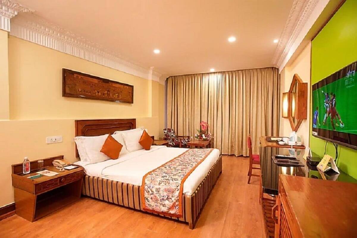 A hotel room with a bed, bedside table, TV, and curtains.