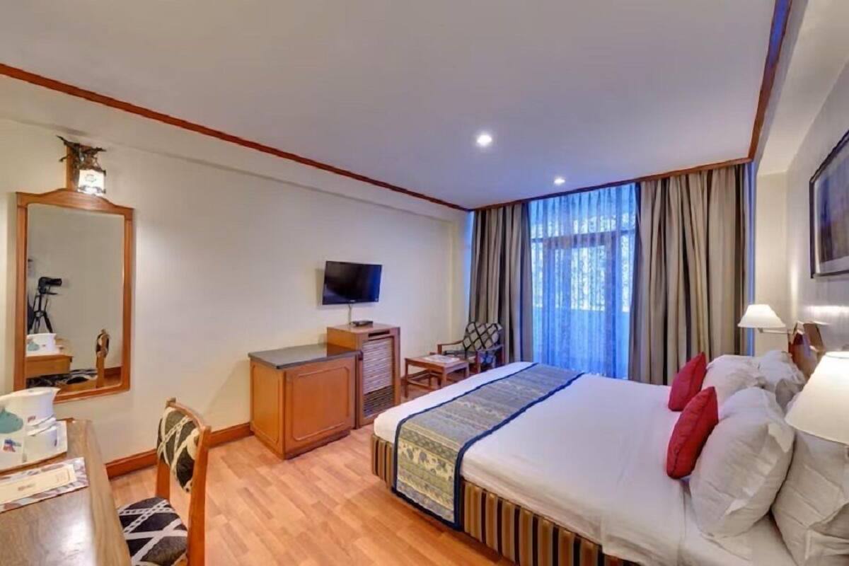 A hotel room with a bed, a desk, a television, and a large window with curtains.