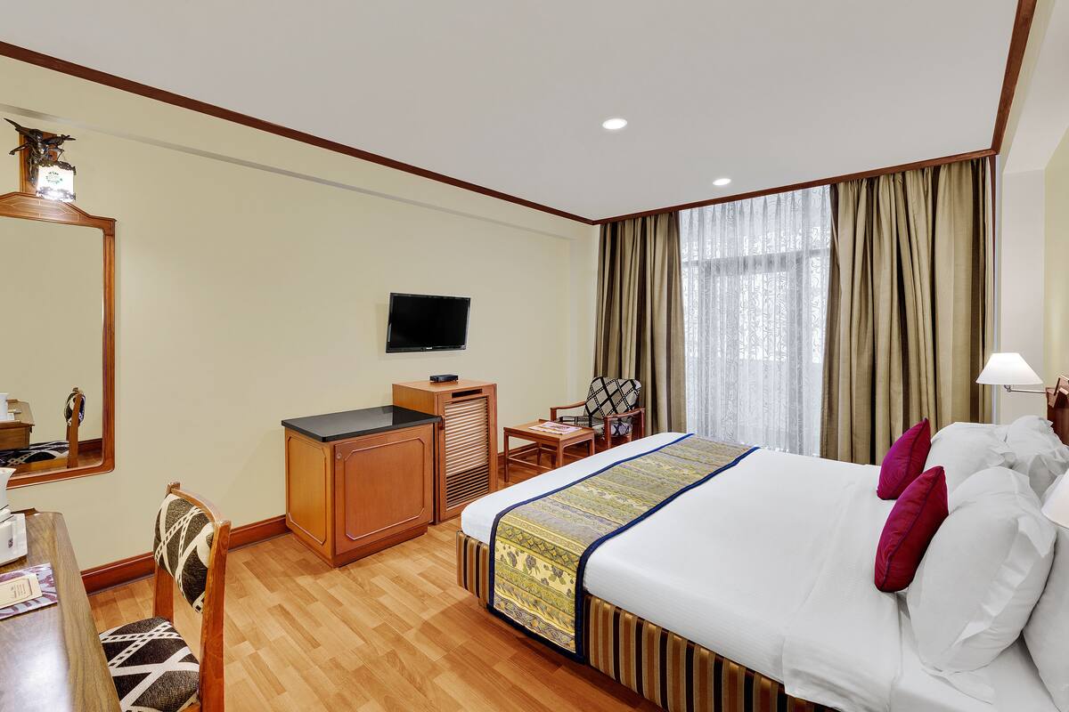 A hotel room with a bed, a desk, a television, a mirror, and a window with curtains.