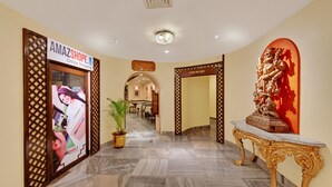 A hotel corridor with a sign for 'AMAZSHOP.COM' on the left, a statue on the right, and a potted plant in the center. - Ambassador Pallava (Chennai)