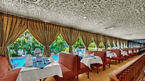 A restaurant with a pool view, red upholstered booths, and white tablecloths. - Ambassador Pallava (Chennai)