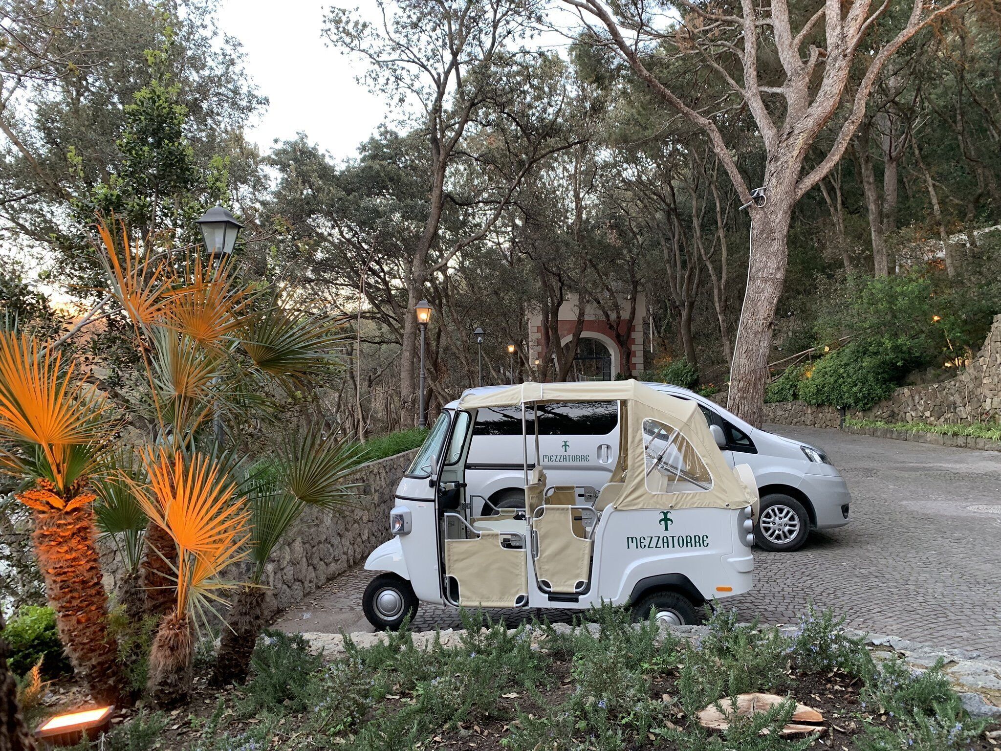 A white golf cart parked on a cobblestone path surrounded by greenery and trees.