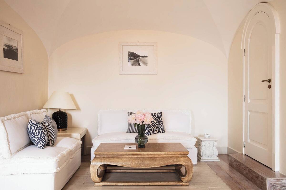 Una sala de estar con un sofá blanco, una mesa de centro con un jarrón de flores, una lámpara y un cuadro en la pared.