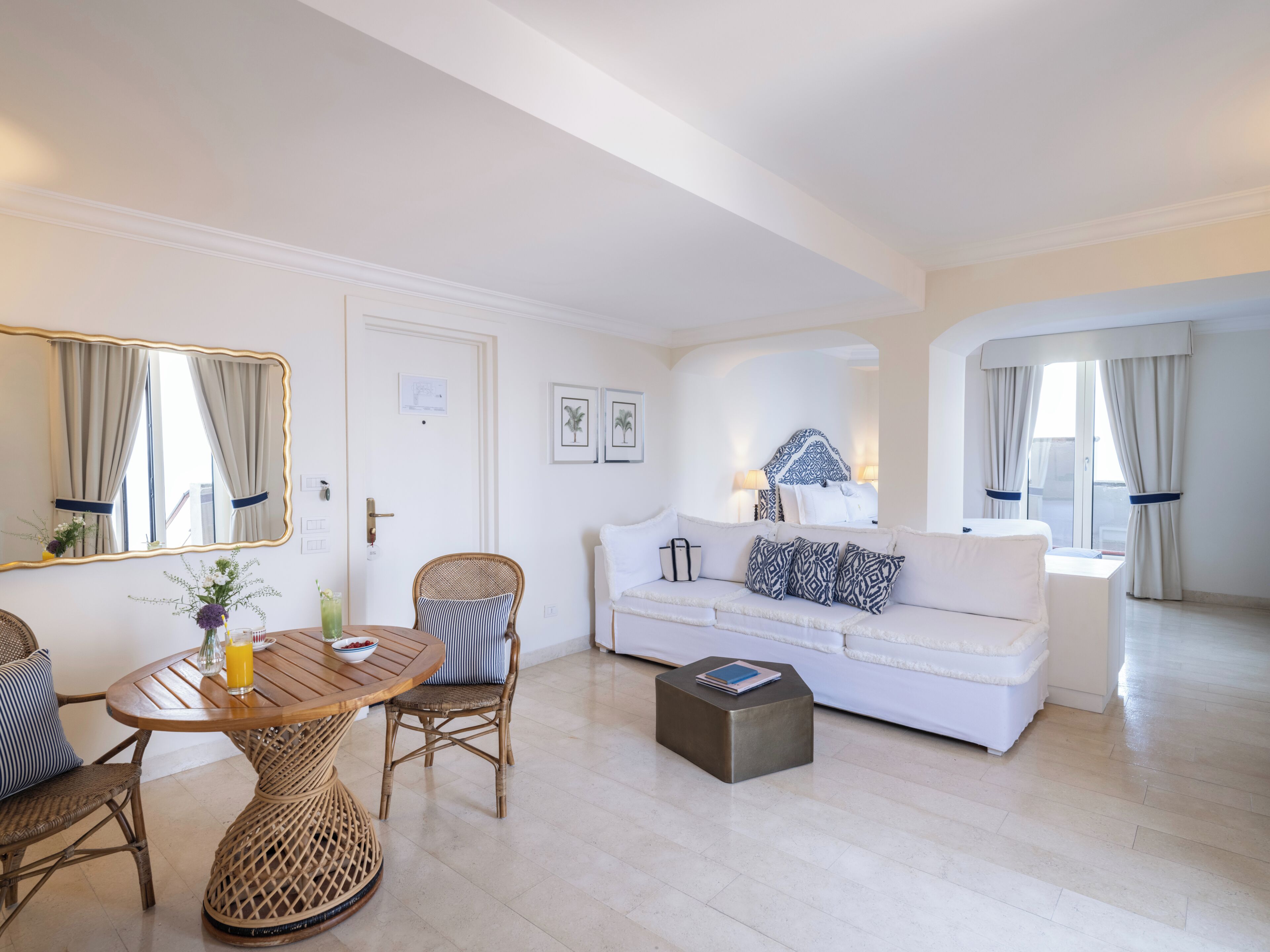 A modern living room with a white sofa, wicker chairs, a round wooden table, and a small coffee table.