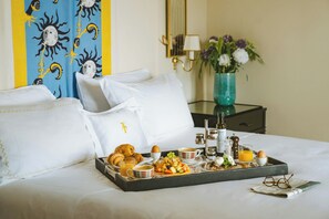 A neatly made bed with white linens, a tray of breakfast including croissants, fruit, and beverages, and a vase with flowers on a bedside table. - Mezzatorre Hotel & Thermal Spa (Forio)