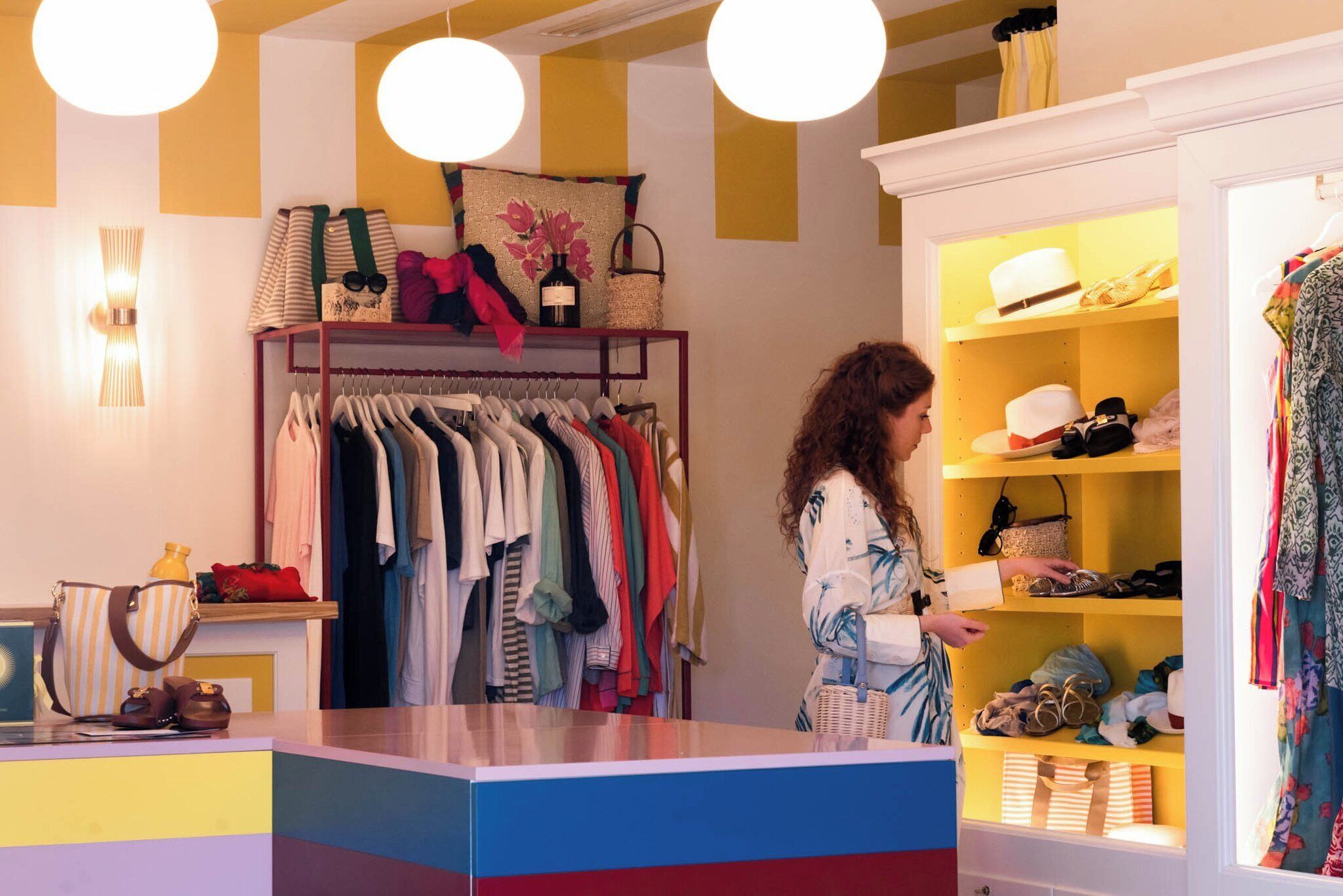Una boutique con ropa variada en perchas y estantes, un mostrador con bolsos, y una persona mirando.