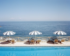 A poolside area with lounge chairs and umbrellas, overlooking a large body of water. - Mezzatorre Hotel & Thermal Spa (Forio)