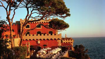 A coastal building with a terrace overlooking the sea, featuring a castle-like facade and outdoor seating.