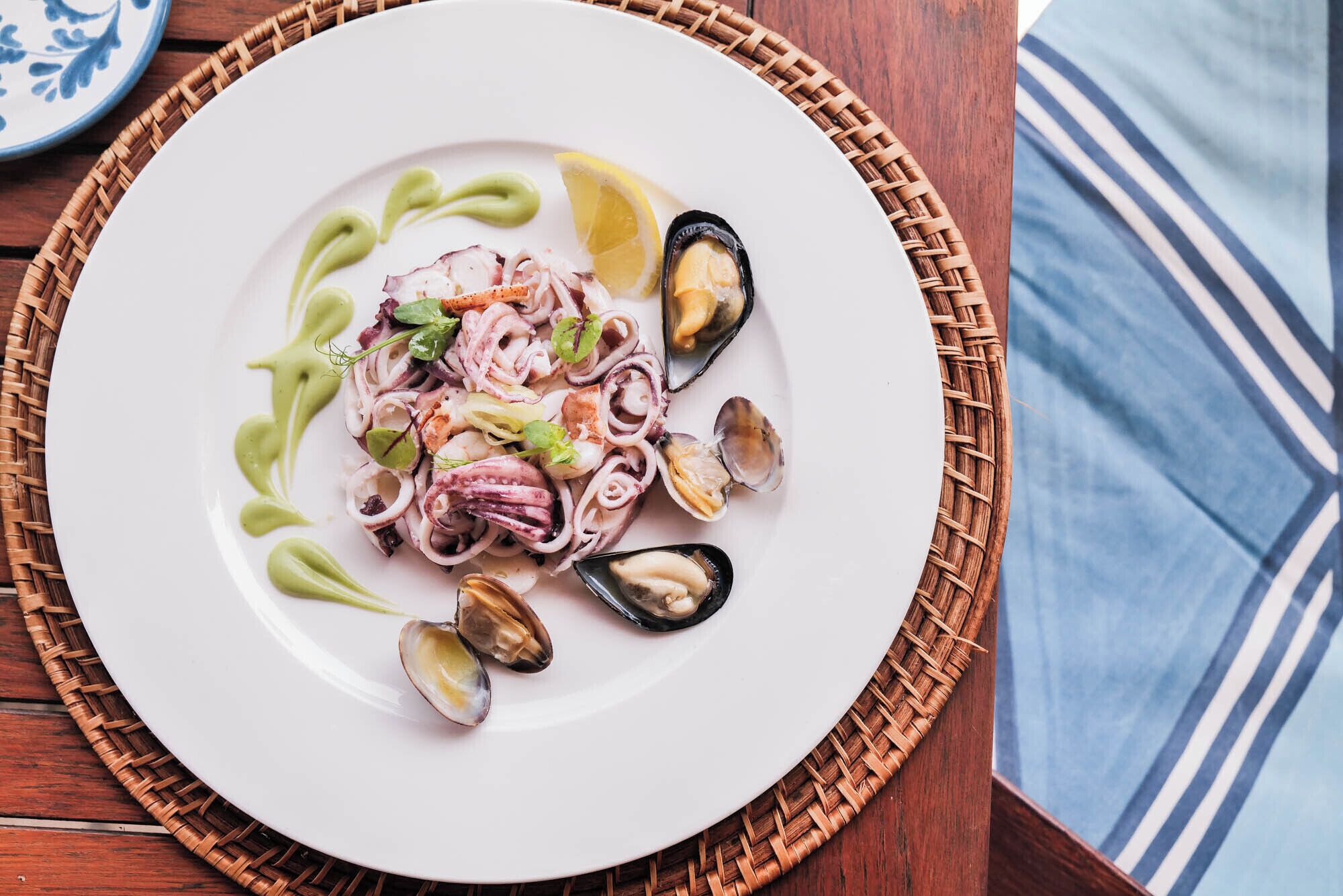 Un plato de mariscos con salsa verde y limón sobre un plato blanco.