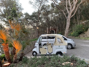 A white golf cart with a beige canopy parked on a cobblestone path surrounded by trees and plants. - Mezzatorre Hotel & Thermal Spa (Forio)