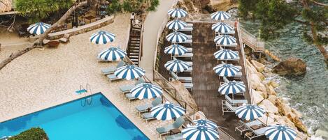 Zona de piscina con múltiples sombrillas, sillas de descanso y una escalera que baja a la playa.