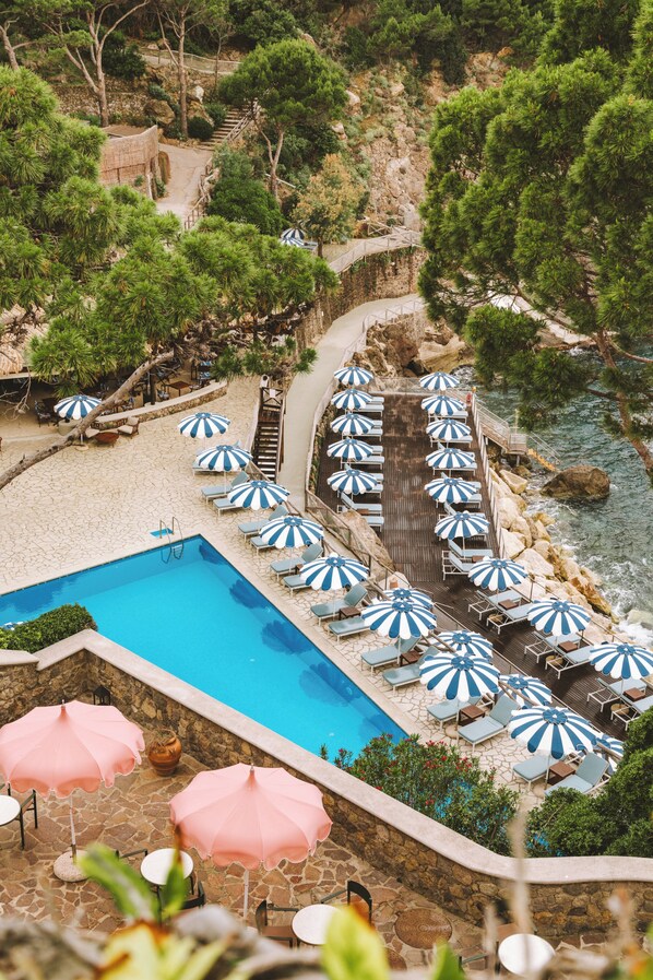 A pool area with multiple umbrellas, lounge chairs, and a staircase leading to a beach.