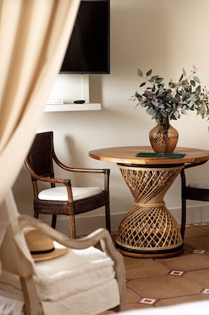 A round wooden table with a woven base, a wicker chair, and a vase with green foliage. - Mezzatorre Hotel & Thermal Spa (Forio)