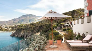 Un balcón con vistas al mar y a las montañas, mobiliario exterior y barandilla de cristal.