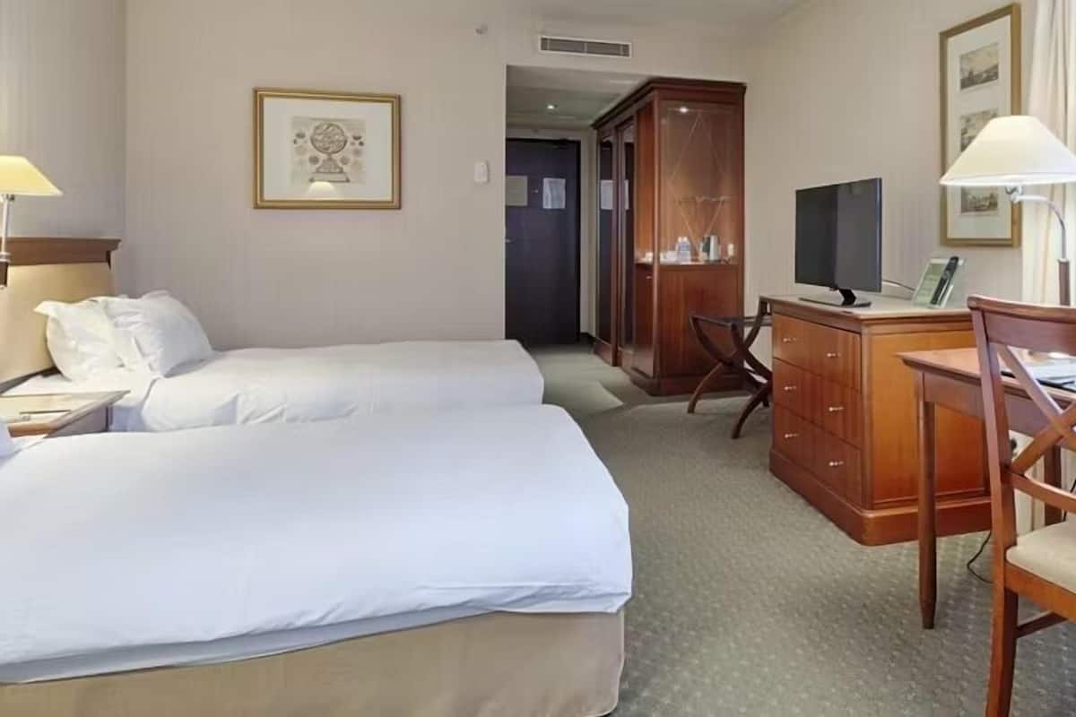A hotel room with two beds, a desk, a chair, a TV, and a wardrobe.