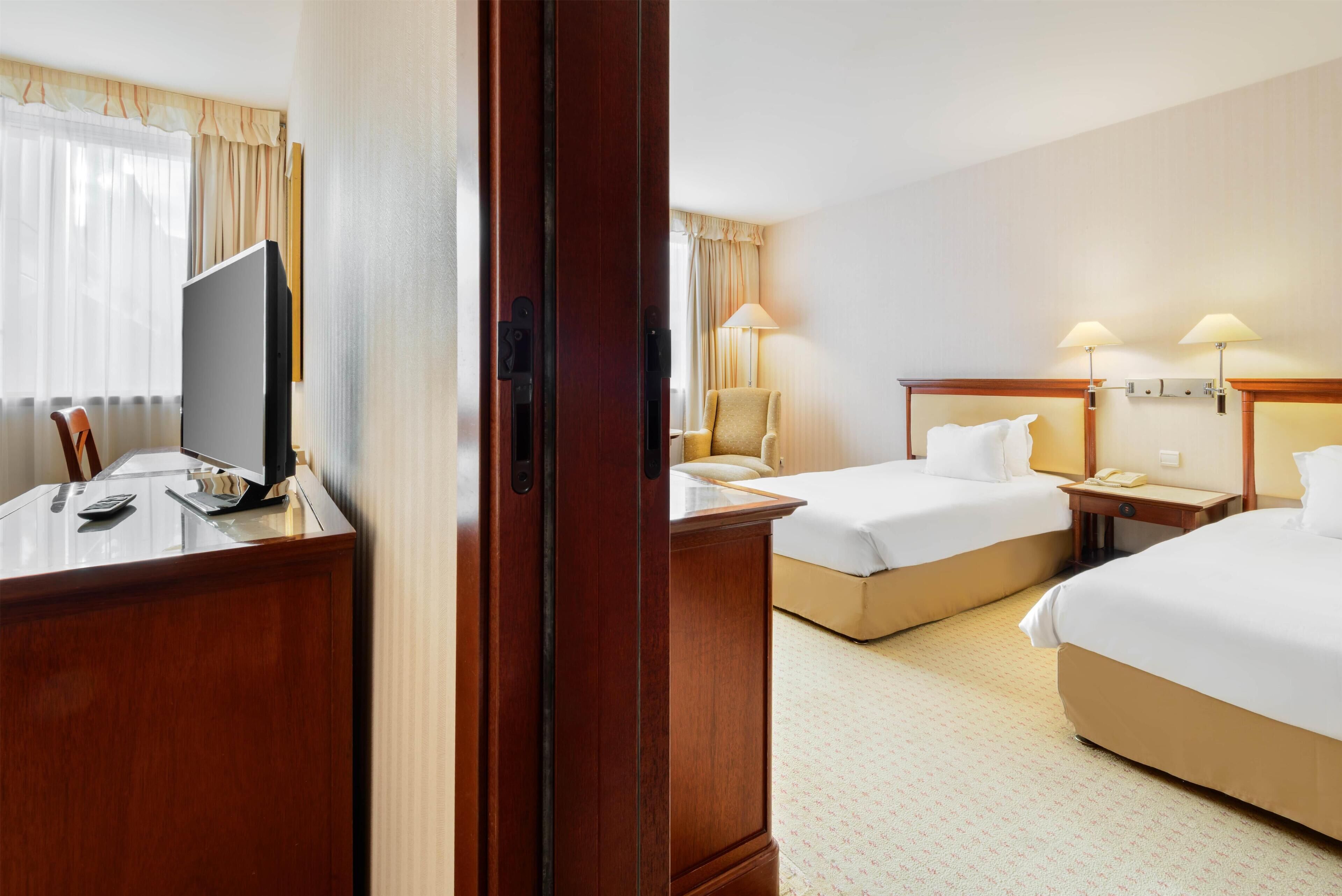 Une chambre d’hôtel équipée d’un bureau, de deux lits, d’une chaise et d’un téléviseur.