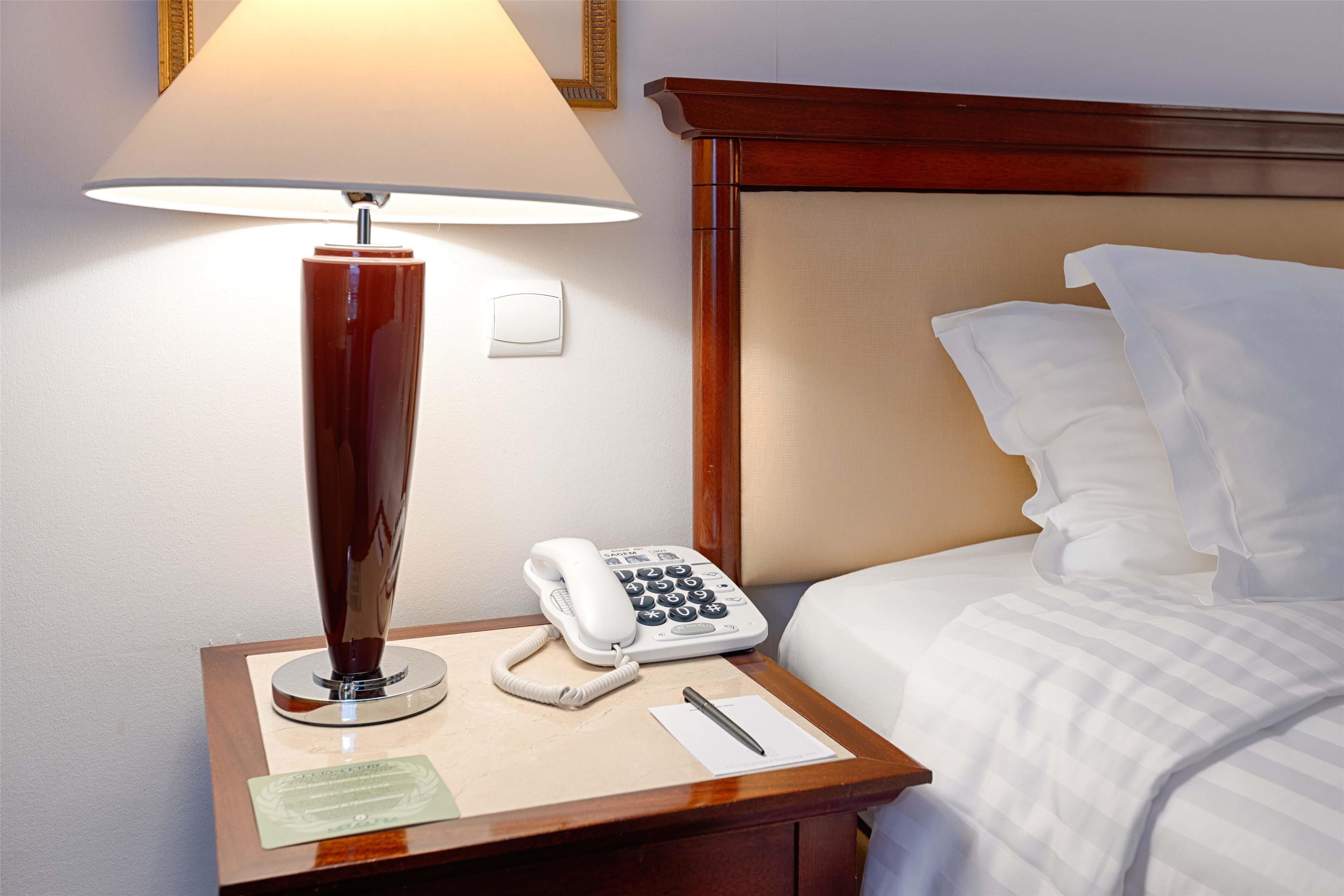 Une chambre d’hôtel équipée d’une lampe de chevet, d’un téléphone, d’un bloc-notes et d’un stylo sur la table de chevet.