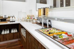 Zona de bufé con diferentes alimentos y dispensador de yogur.