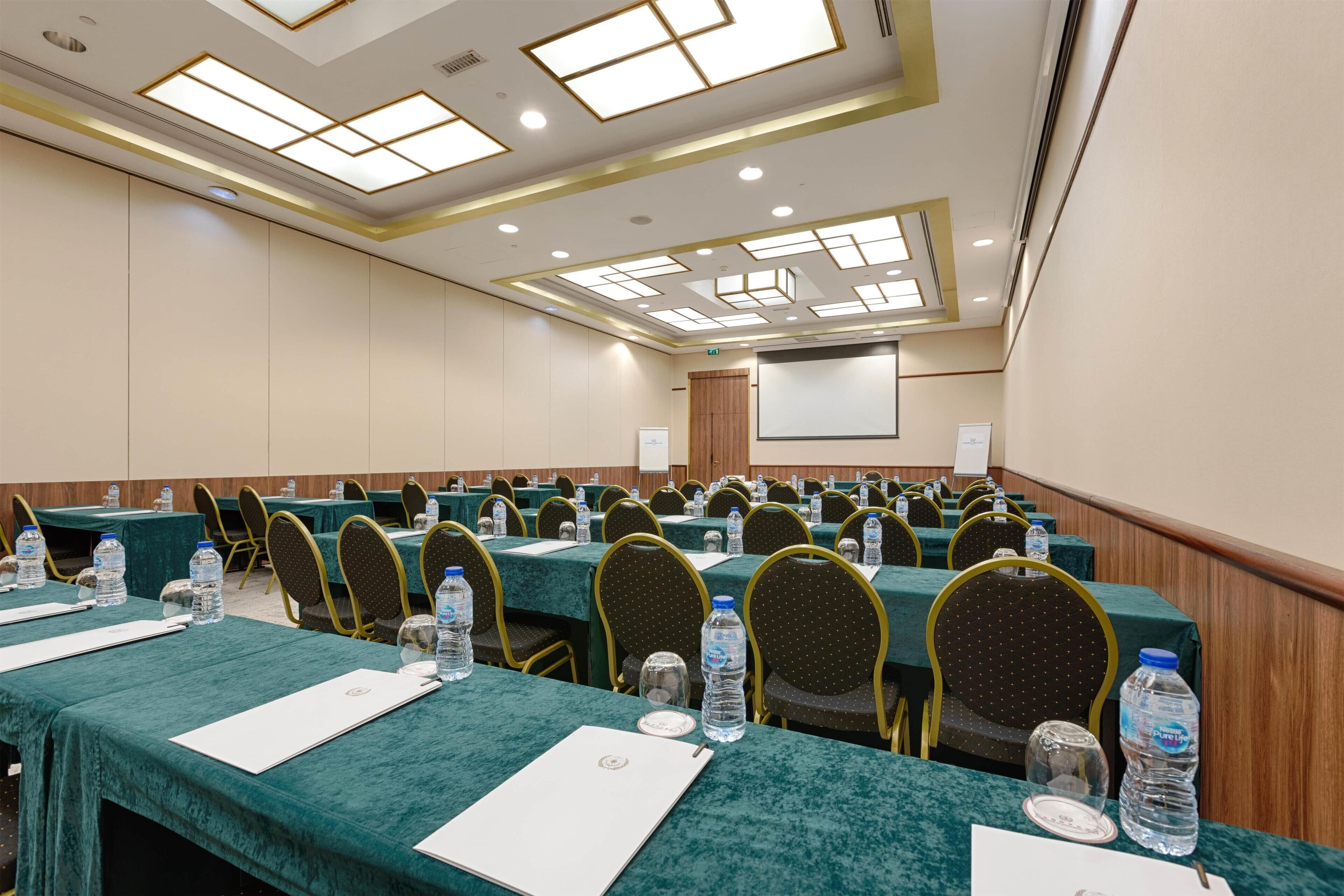 Un salón de conferencias con filas de mesas, sillas y botellas de agua.