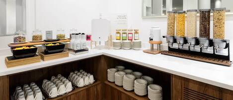 A breakfast buffet setup with various food items and drink dispensers.