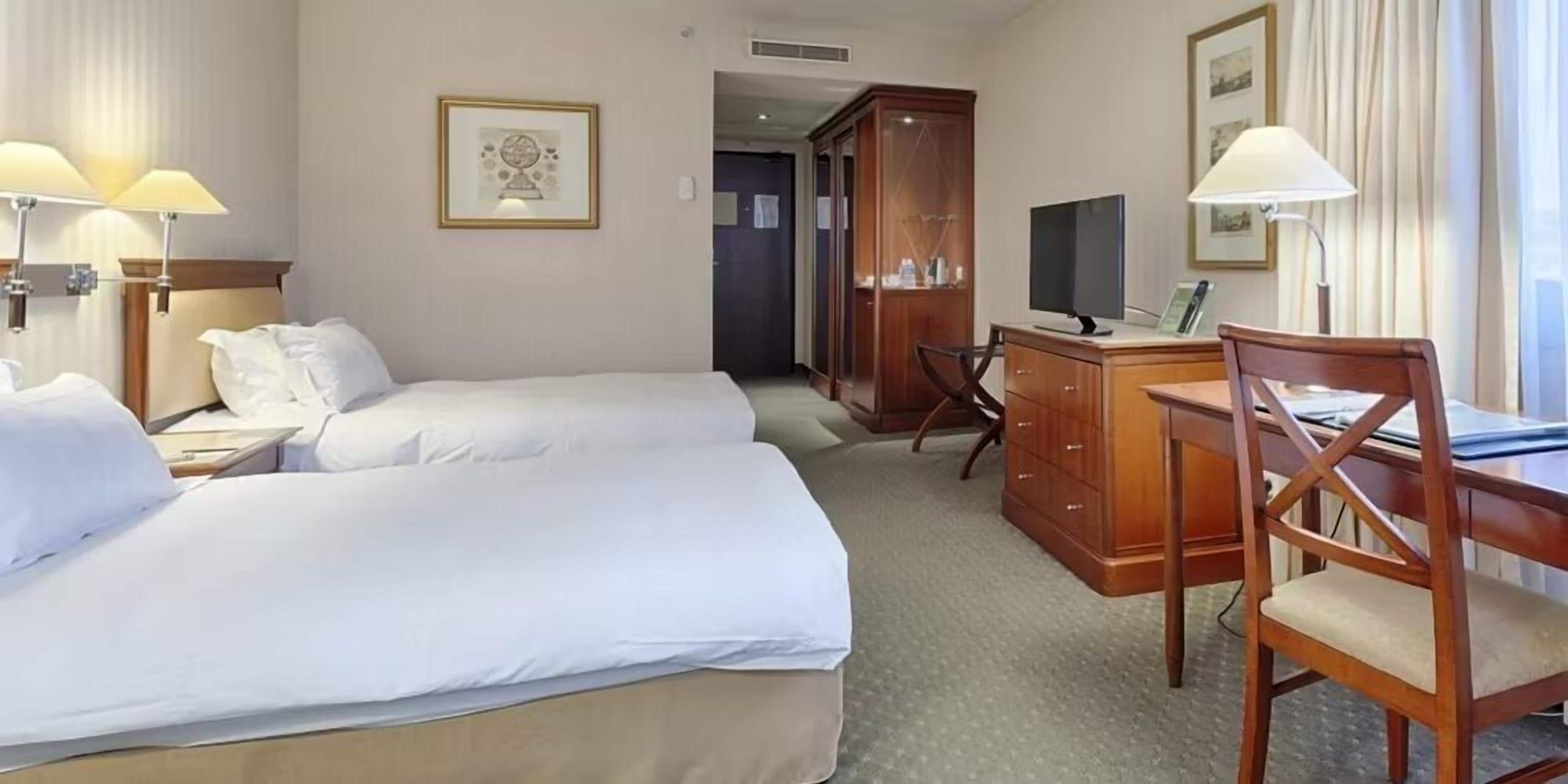 A hotel room with two beds, a desk, a chair, a TV, and a wardrobe.