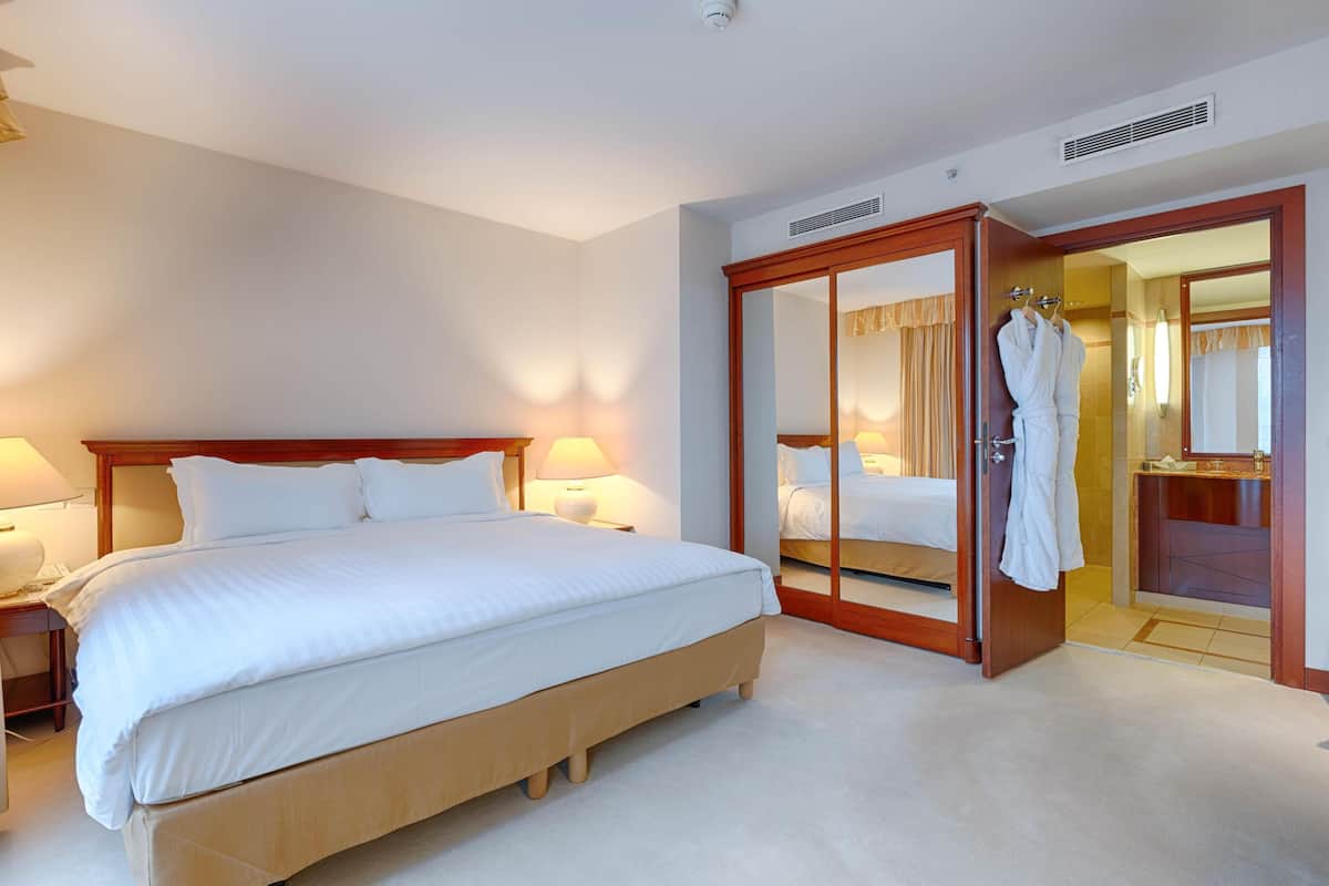 A hotel room with a large bed, bedside lamps, a wardrobe with a mirror, and a bathroom visible through an open door.