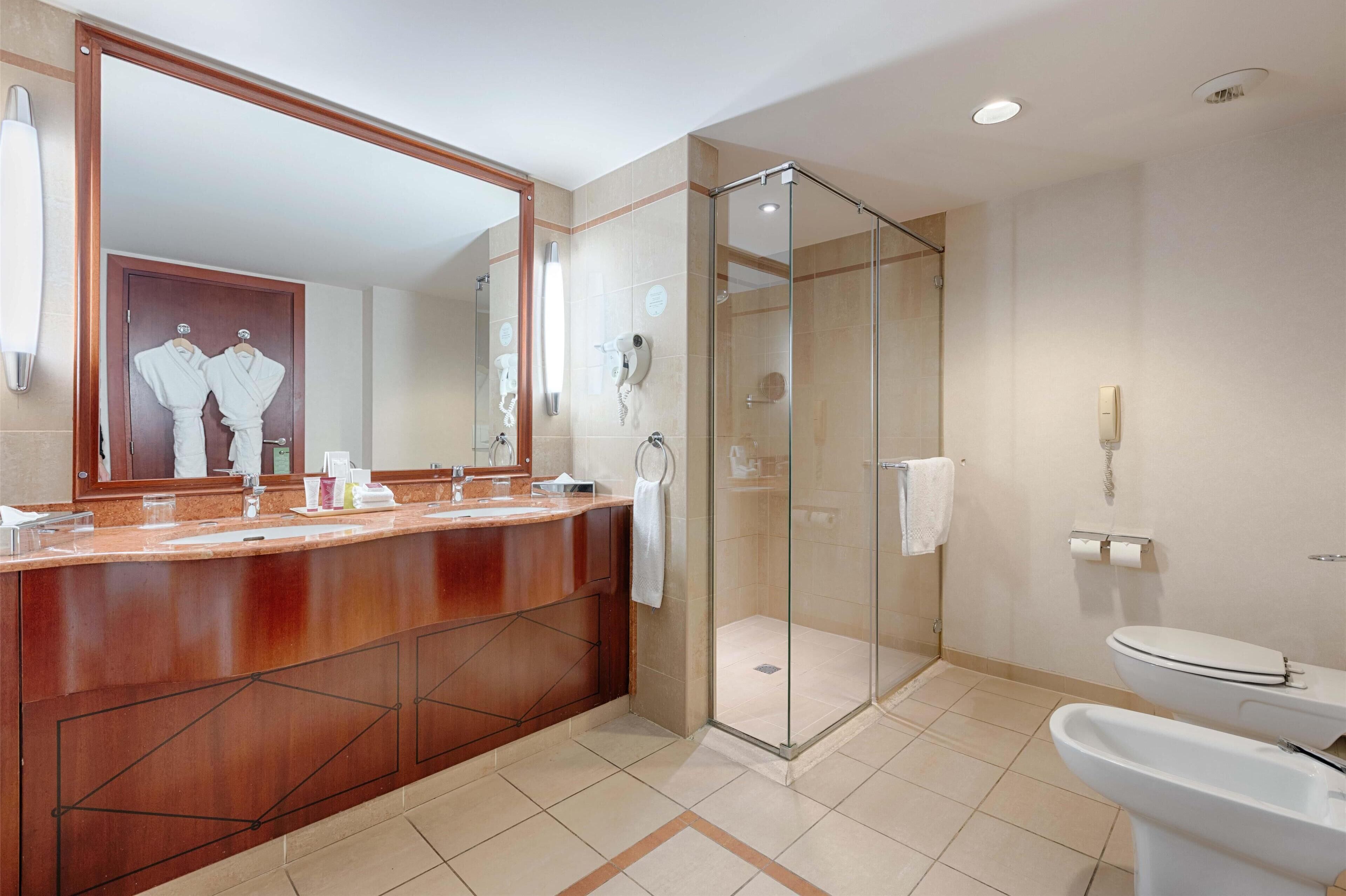 Een moderne badkamer met een houten wastafelmeubel, een glazen douchecabine en een wit toilet.