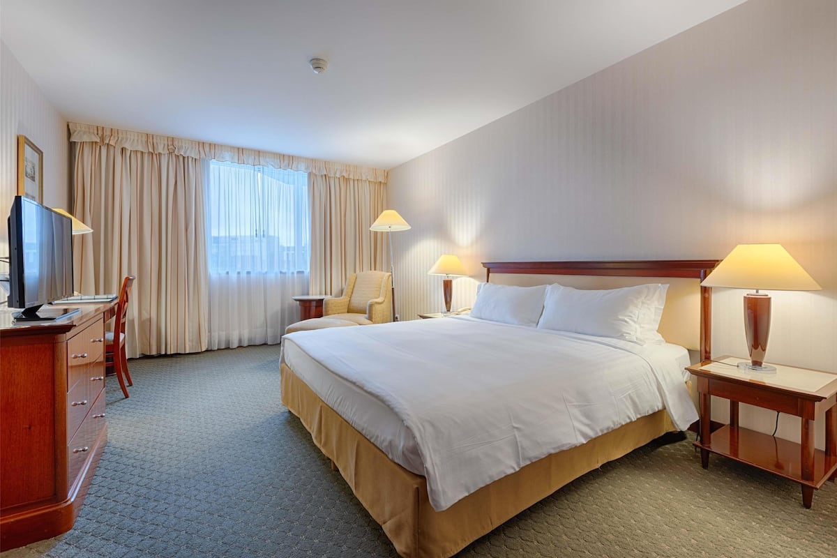 A hotel room with a large bed, two bedside tables with lamps, a desk with a TV, and a chair.