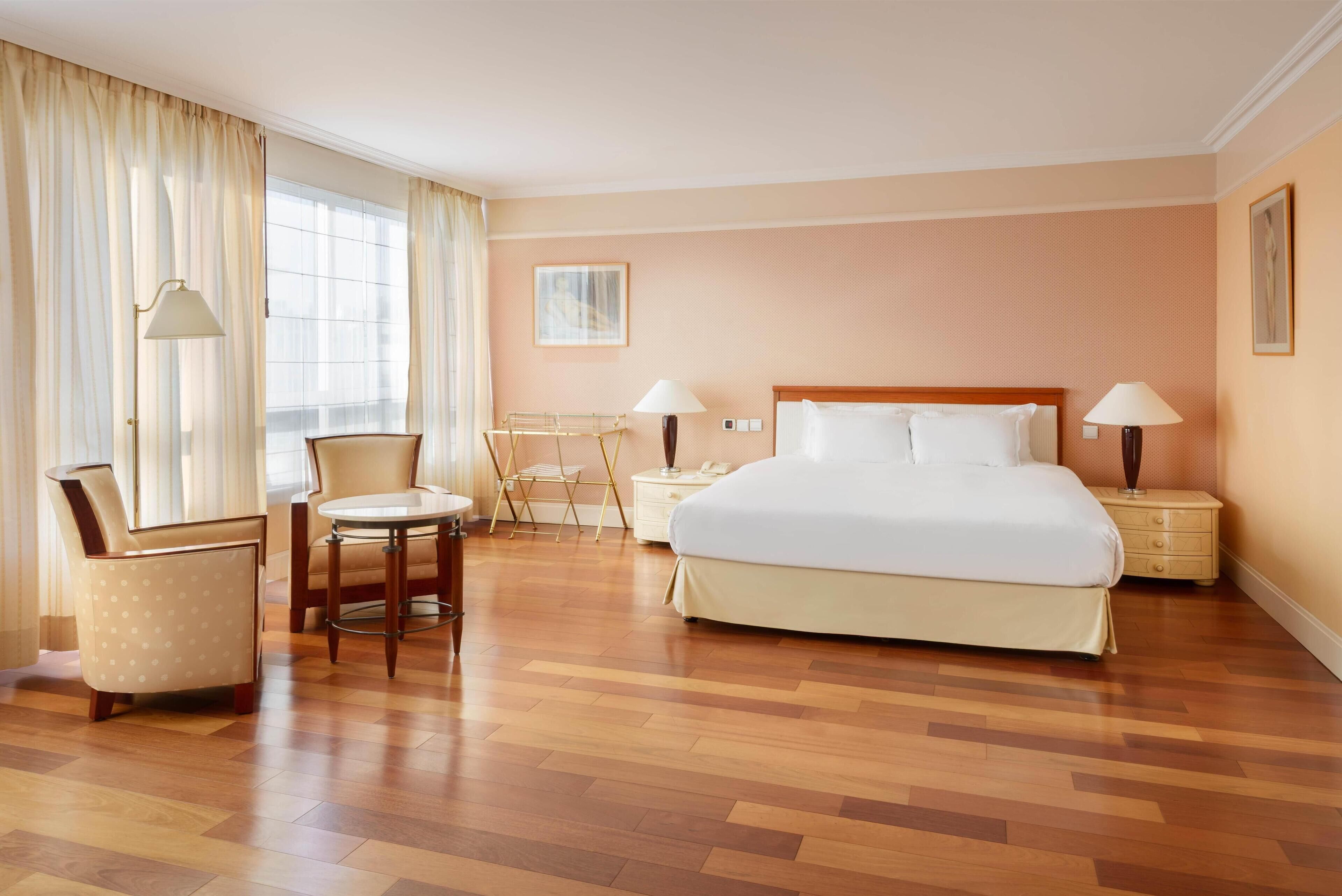 A hotel room with a large bed, a chair, a small table, and two bedside lamps.