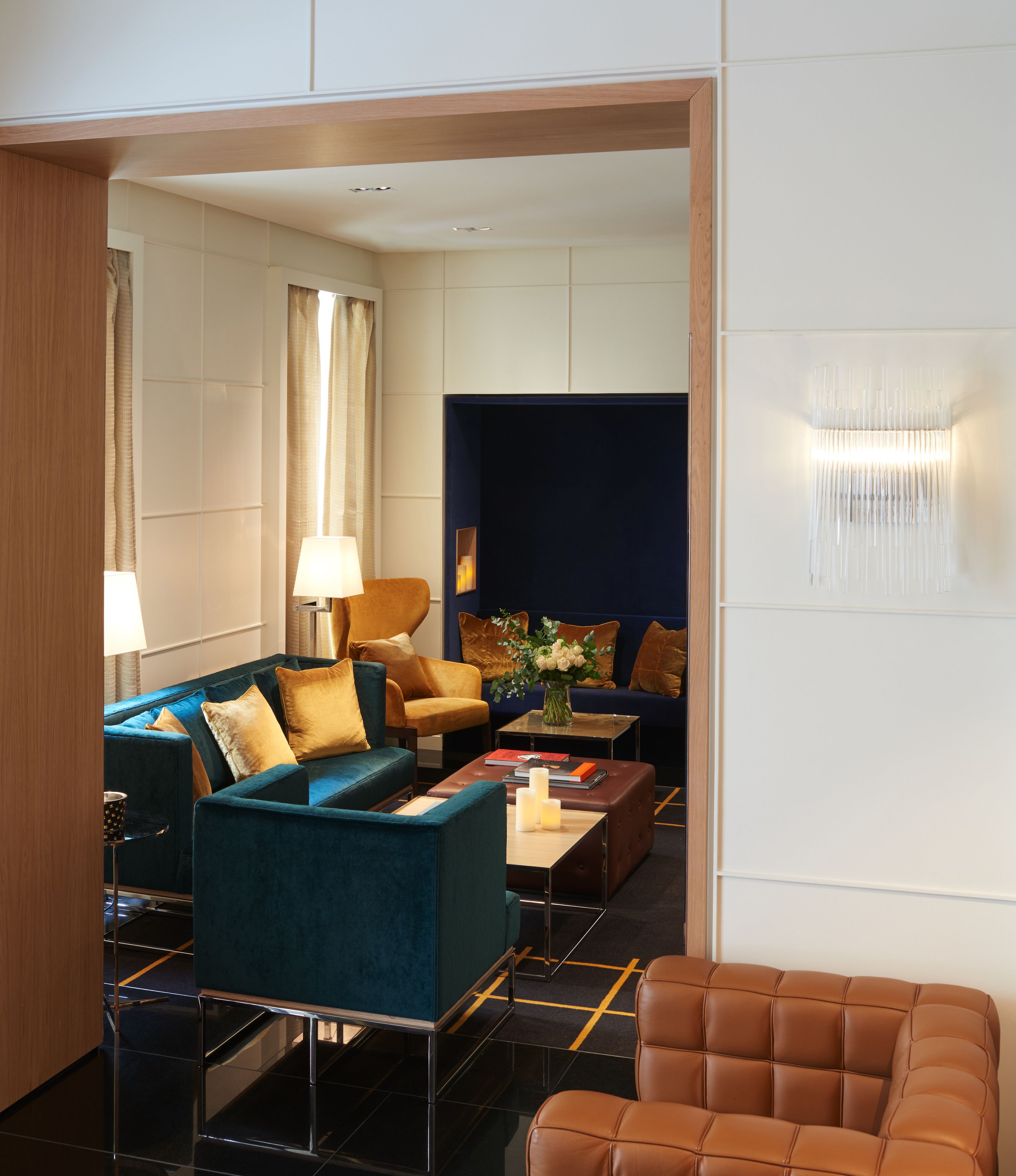 A modern hotel room with a blue sofa set, a brown leather armchair, and a small coffee table with a vase.