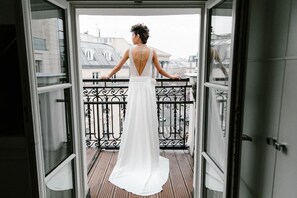 A woman in a white dress standing on a balcony with a wrought iron railing, overlooking a cityscape. - Hôtel Opéra Richepanse (Paris)