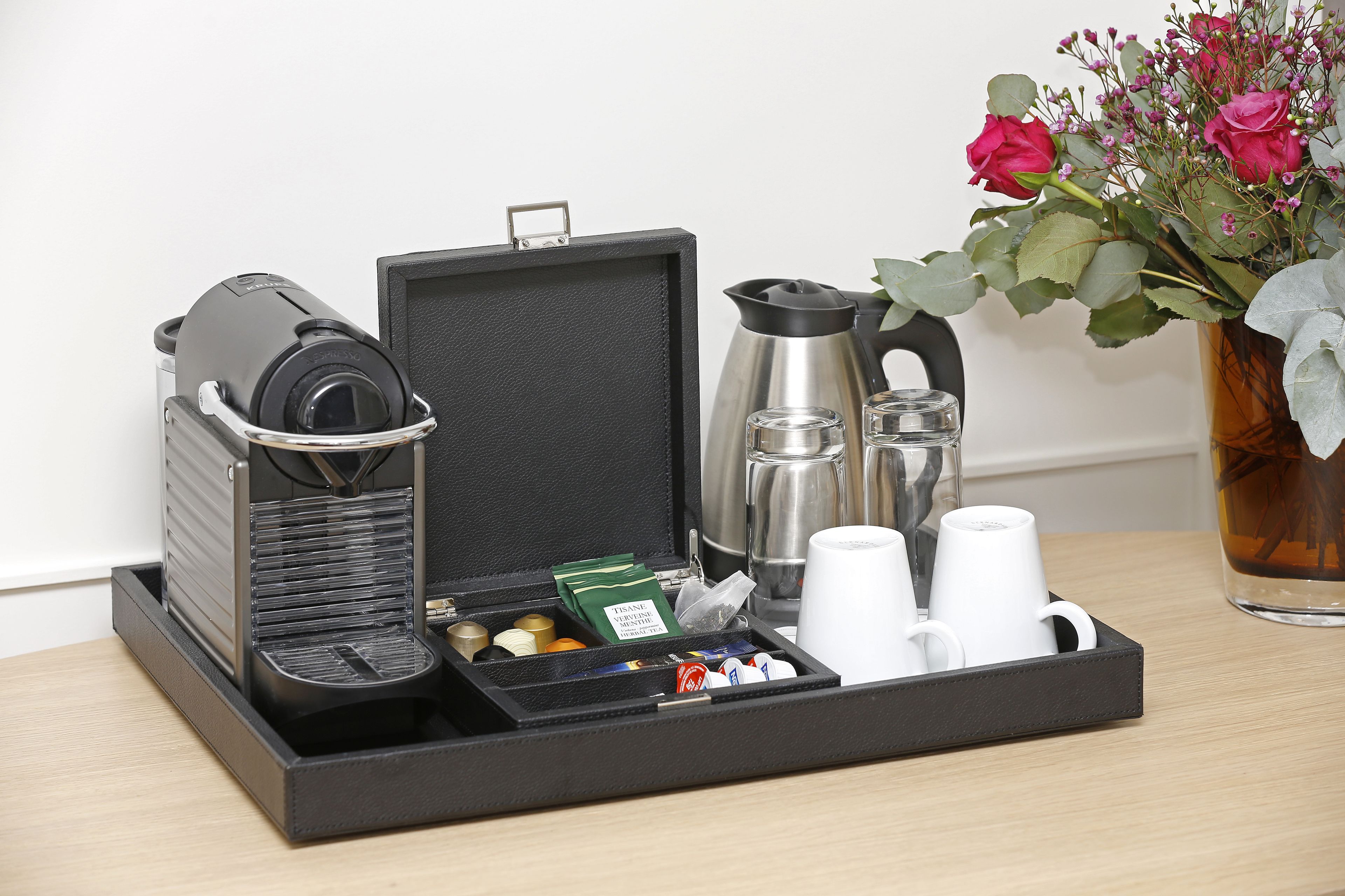 A coffee maker, a kettle, a tray with cups and a vase of flowers on a table.