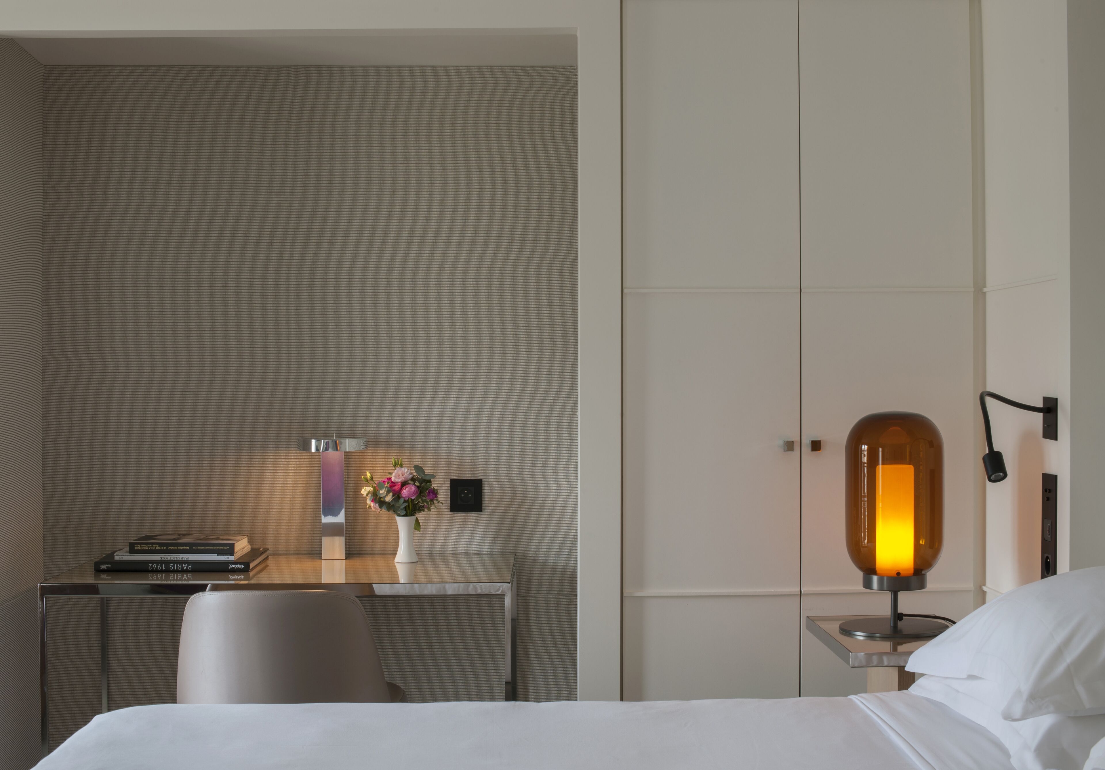 Een hotelkamer met een bed, een bureau met lamp, een stoel en een tafeltje met een bloevas.