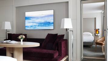 Una habitación de hotel moderna con un ventanal grande, un sofá, una mesa con un libro y un jarrón, y una cama con una mesita de noche y una lámpara.