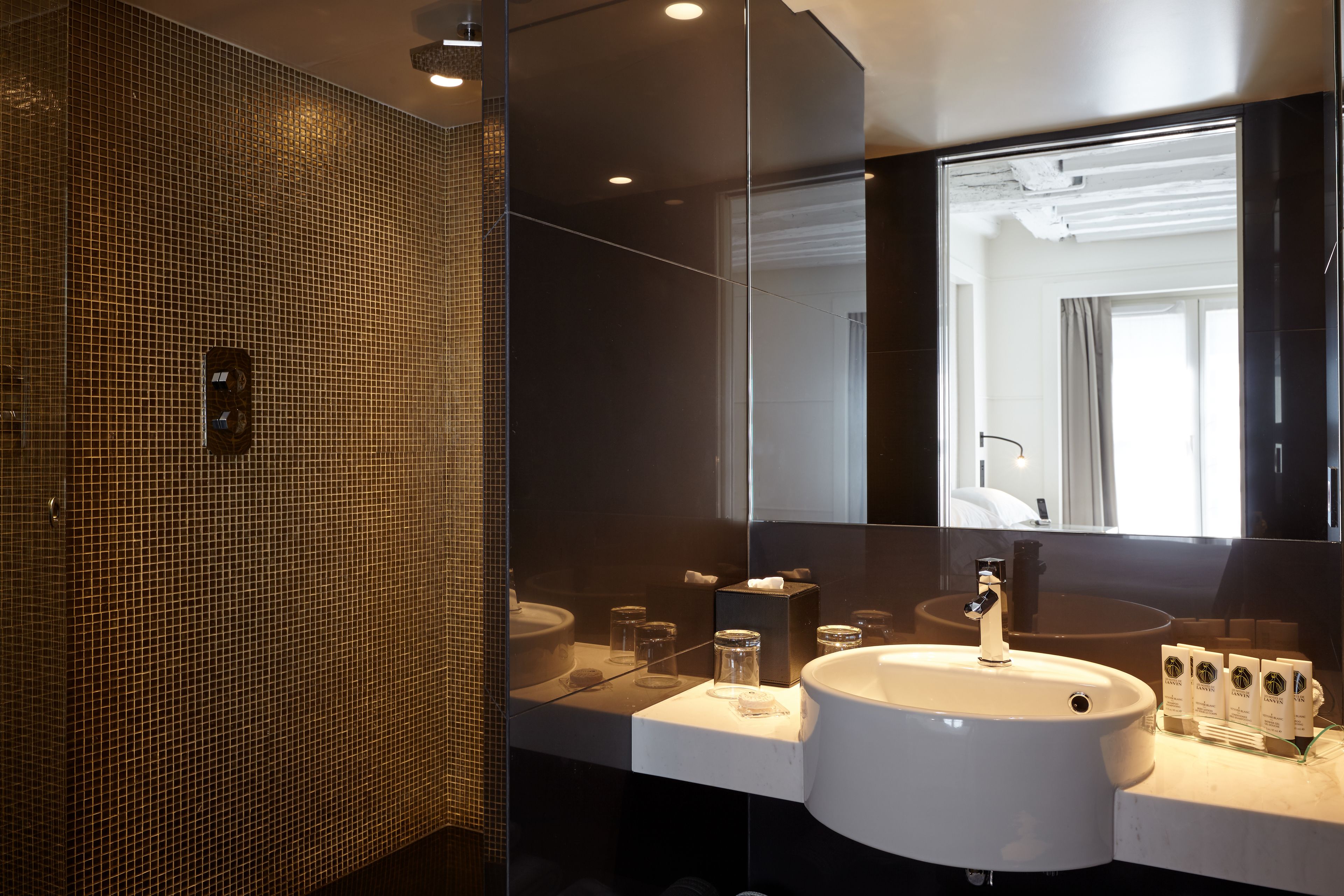 A modern bathroom with a large mirror, a white sink, and a glass shower enclosure.