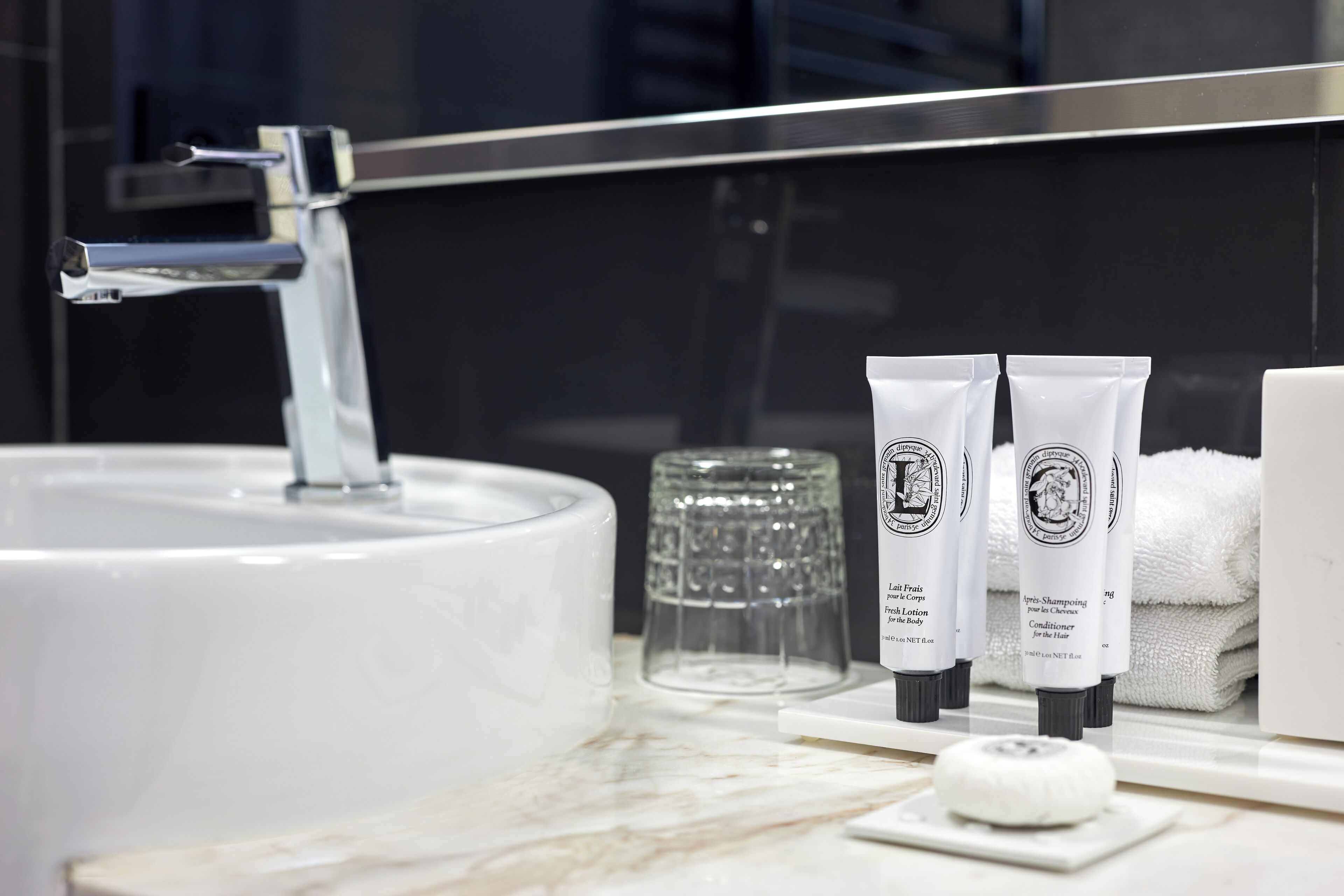 A bathroom with a white sink, a glass container, and two tubes of hair care product.