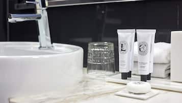 A bathroom with a white sink, a glass container, and two tubes of hair care product.