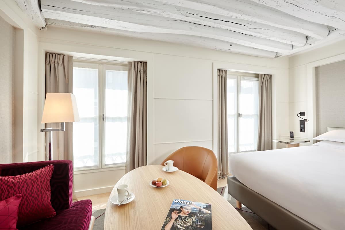 A hotel room with a bed, a desk with a lamp, a chair, a sofa, and a window with curtains.