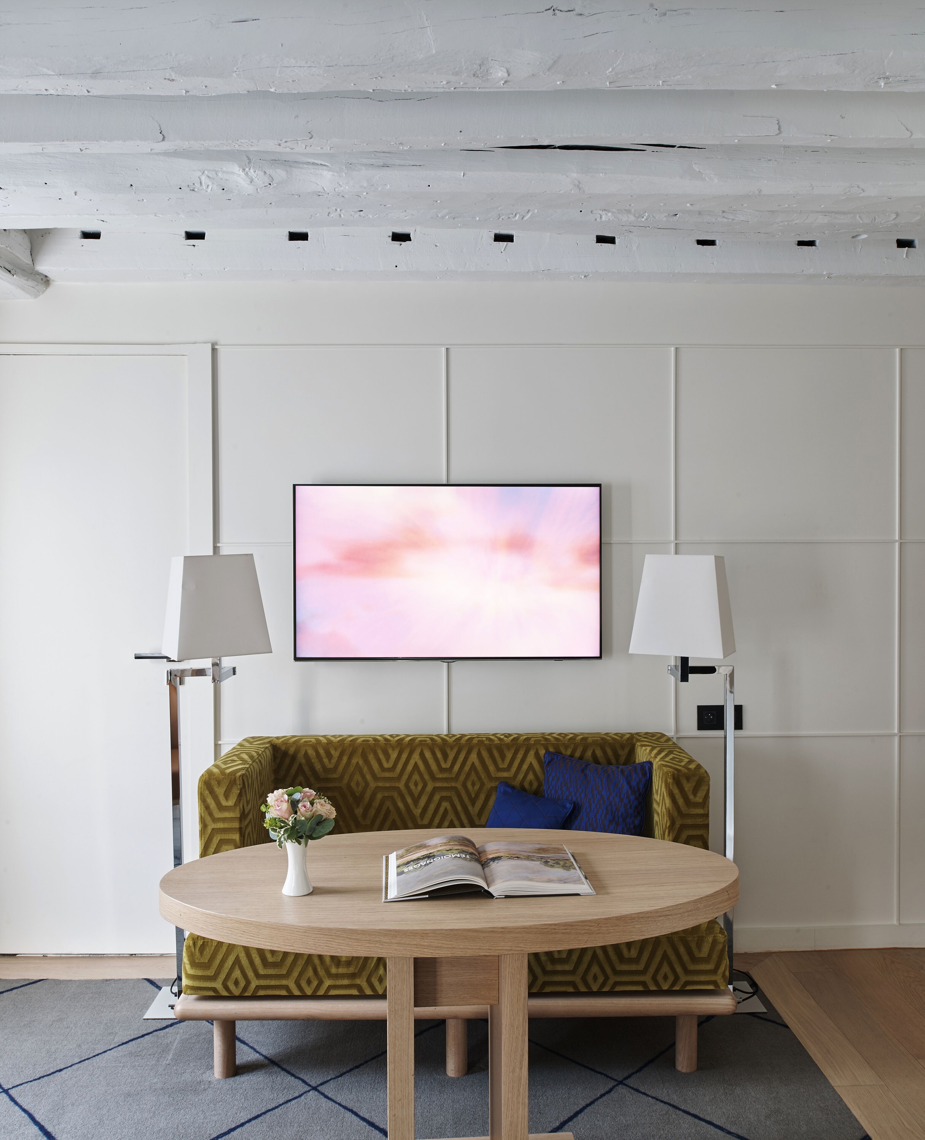 A modern living room with a round wooden table, a sofa with patterned cushions, and two floor lamps.
