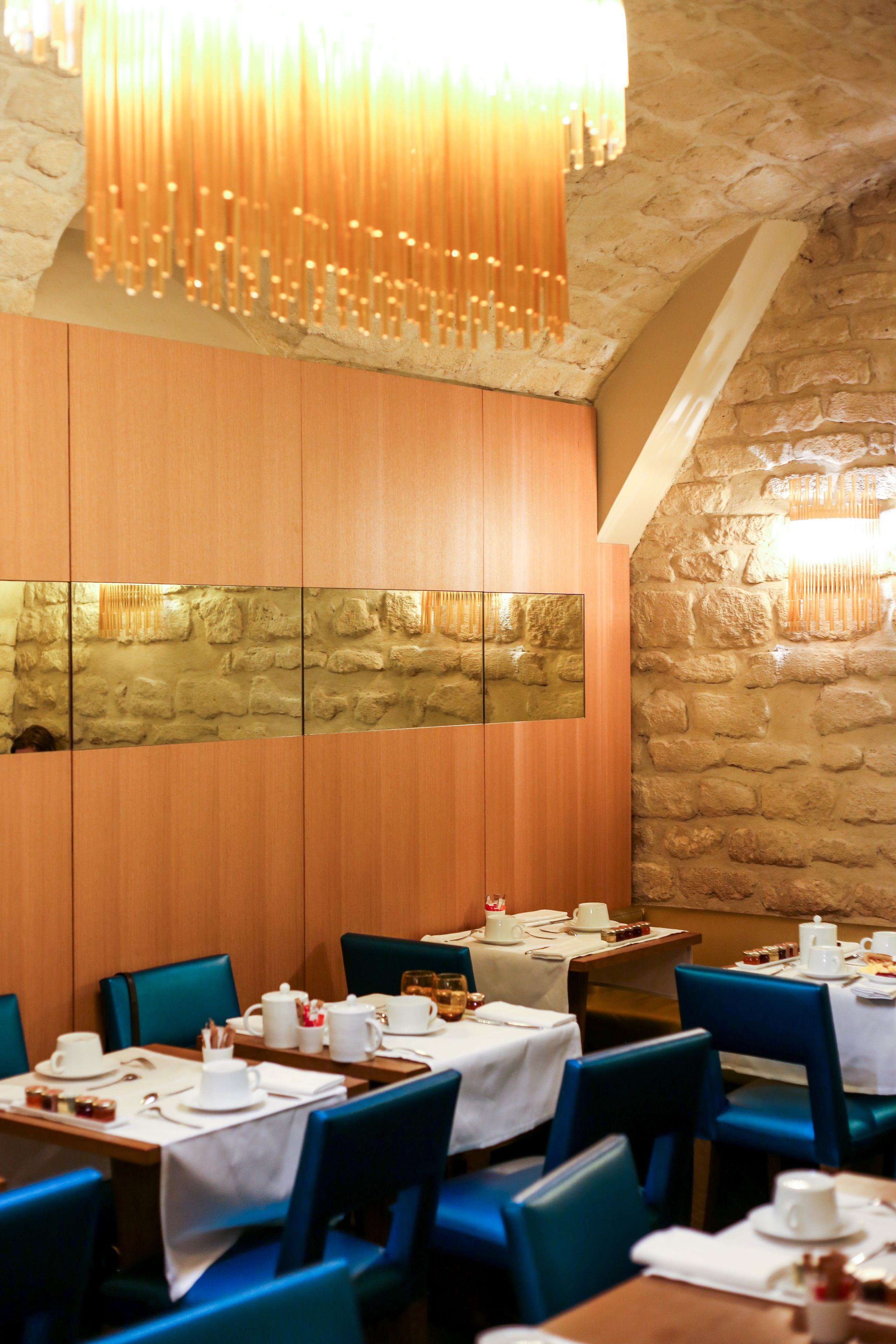 A restaurant with wooden panel walls, stone walls, and blue chairs. Tables are set with white tablecloths and various dishes.