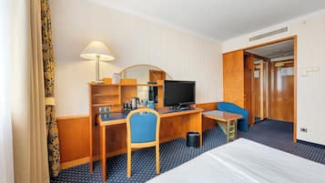 A hotel room with a bed, a desk with a computer, a chair, a television, and a wardrobe.