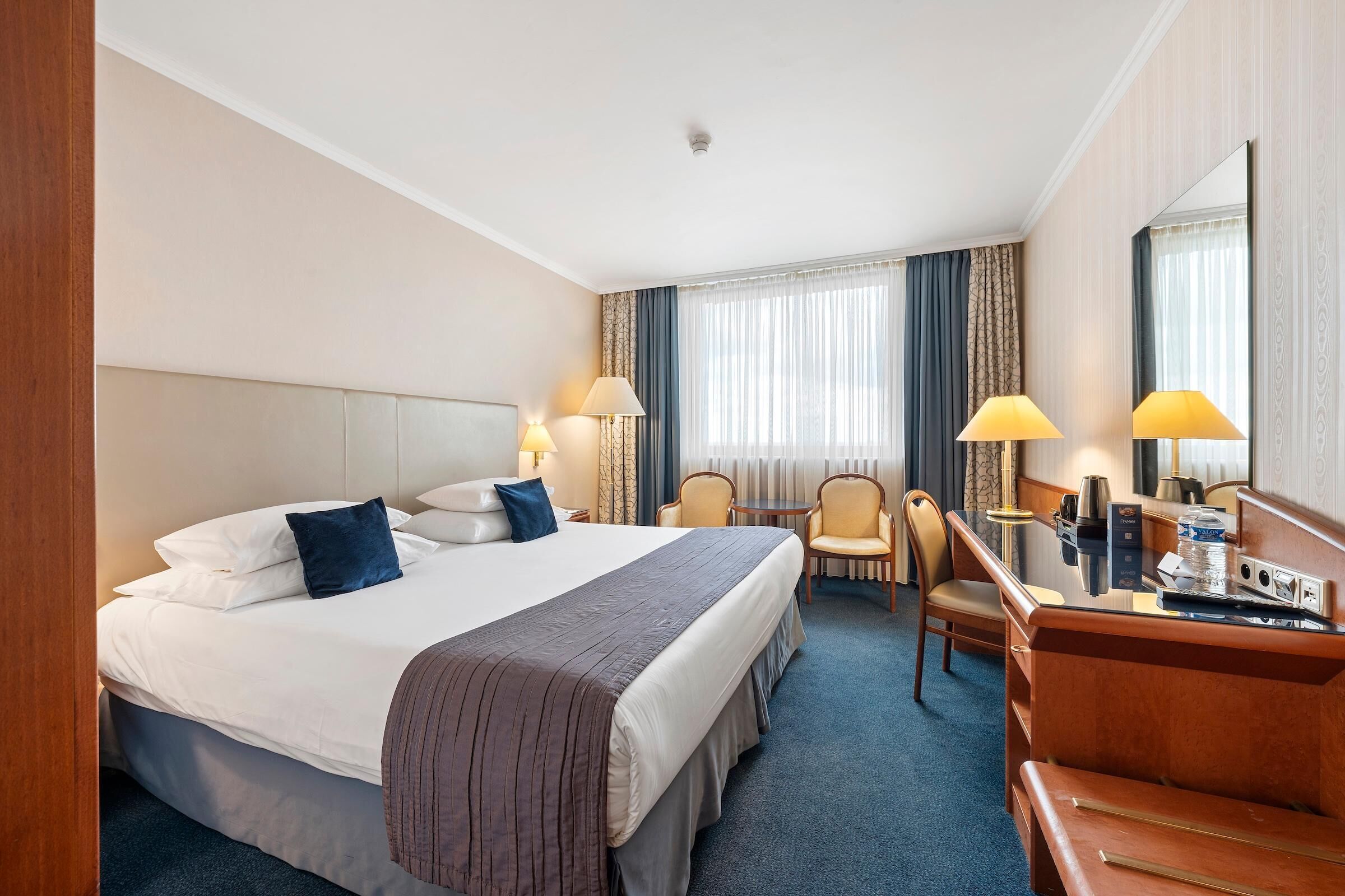 Habitación de hotel con cama, escritorio, sillas y un espejo grande.